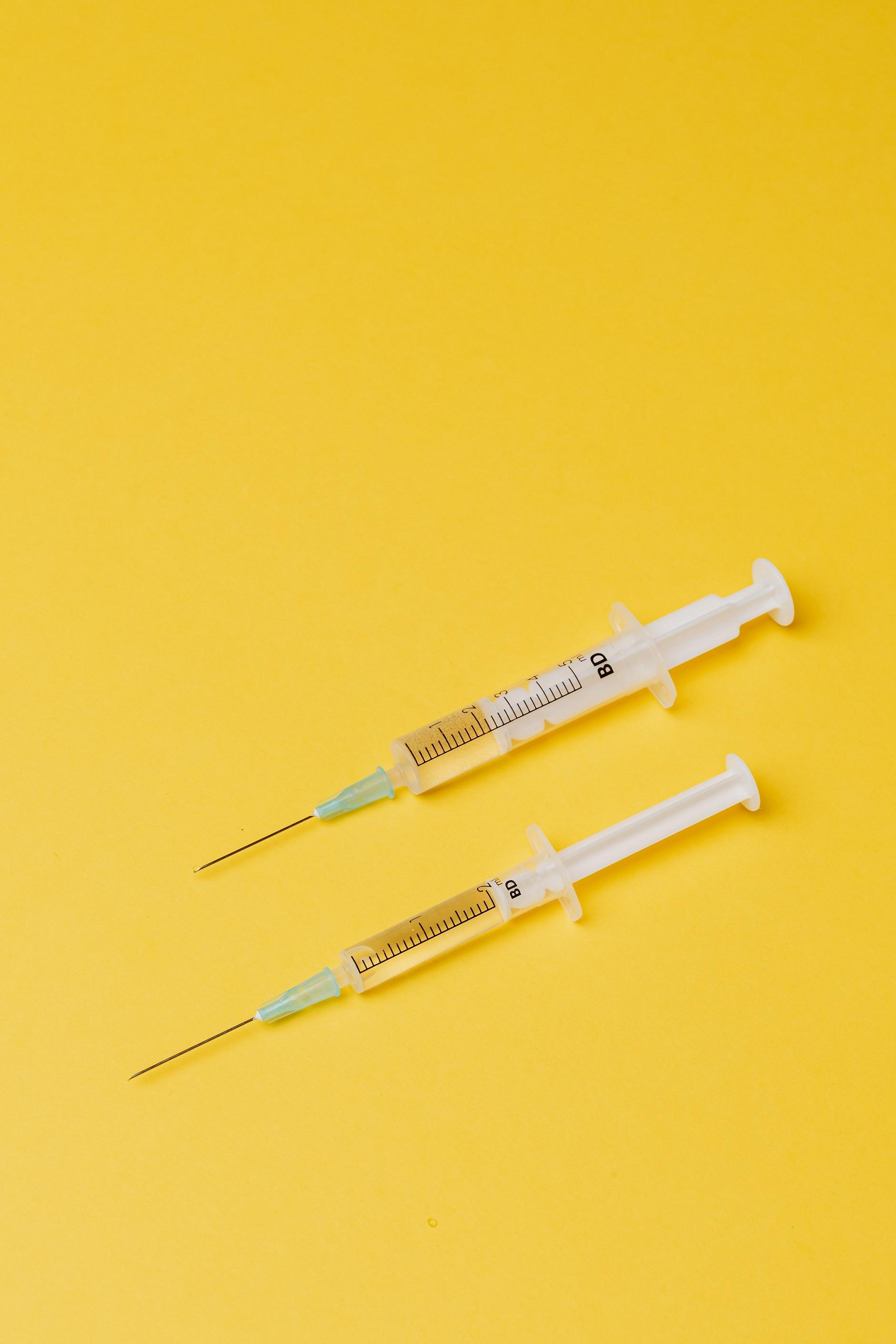 Zwei Spritzen // Impfen auf gelbem Grund